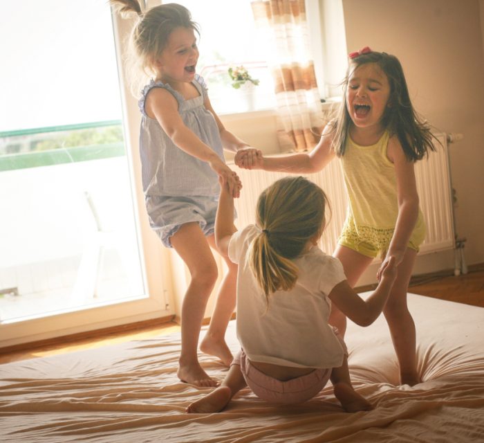 Three children holding hands and jumping on bed laughing