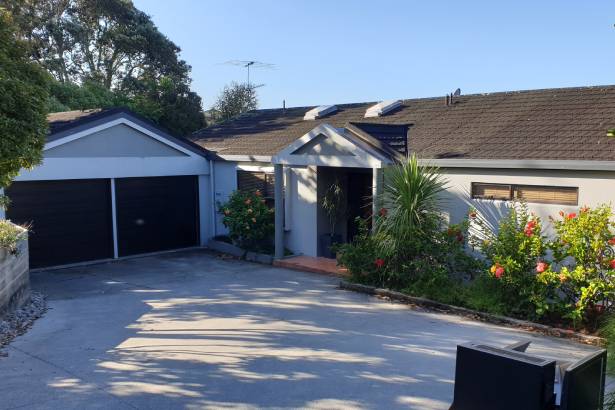 White home with dark coloured roof, and a double garage. Garden with trees at the front of the home